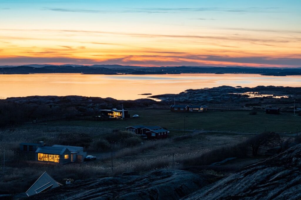 Breathtaking sunset over a rural coastal area with illuminated houses and serene water views.